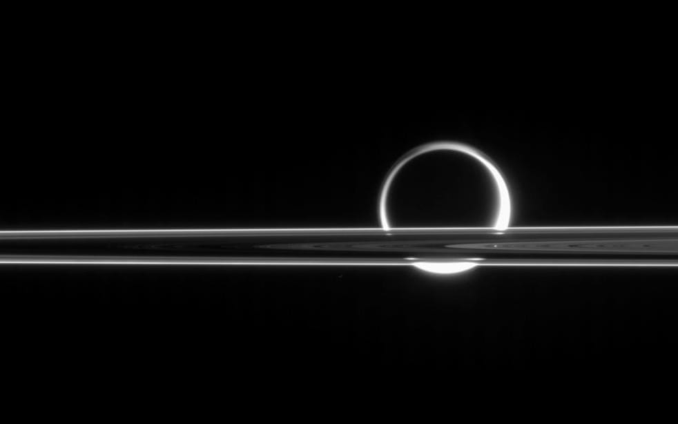 Saturn's rings slice across the moon Titan, its hazy atmosphere illuminated from behind almost like a crescent moon in this black and white photo from the Cassini spacecraft